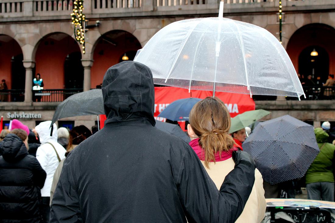 En mann og en dame st&aring;r med ryggen til, han har en arm over skulderen hennes, de deler en paraply